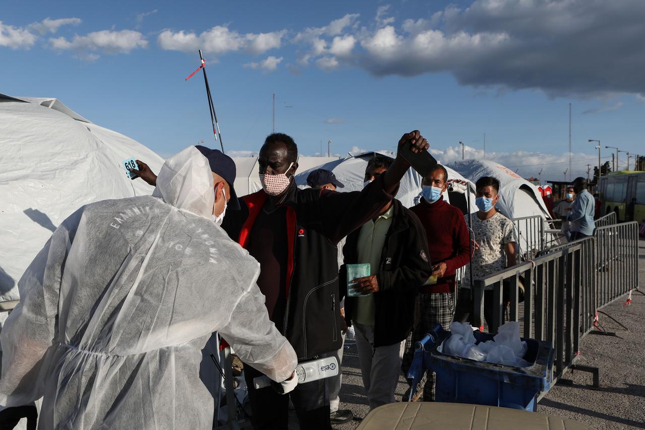 A police officer conducts  checks on refugees and migrants before entering a temporary camp on the island of Lesbos
