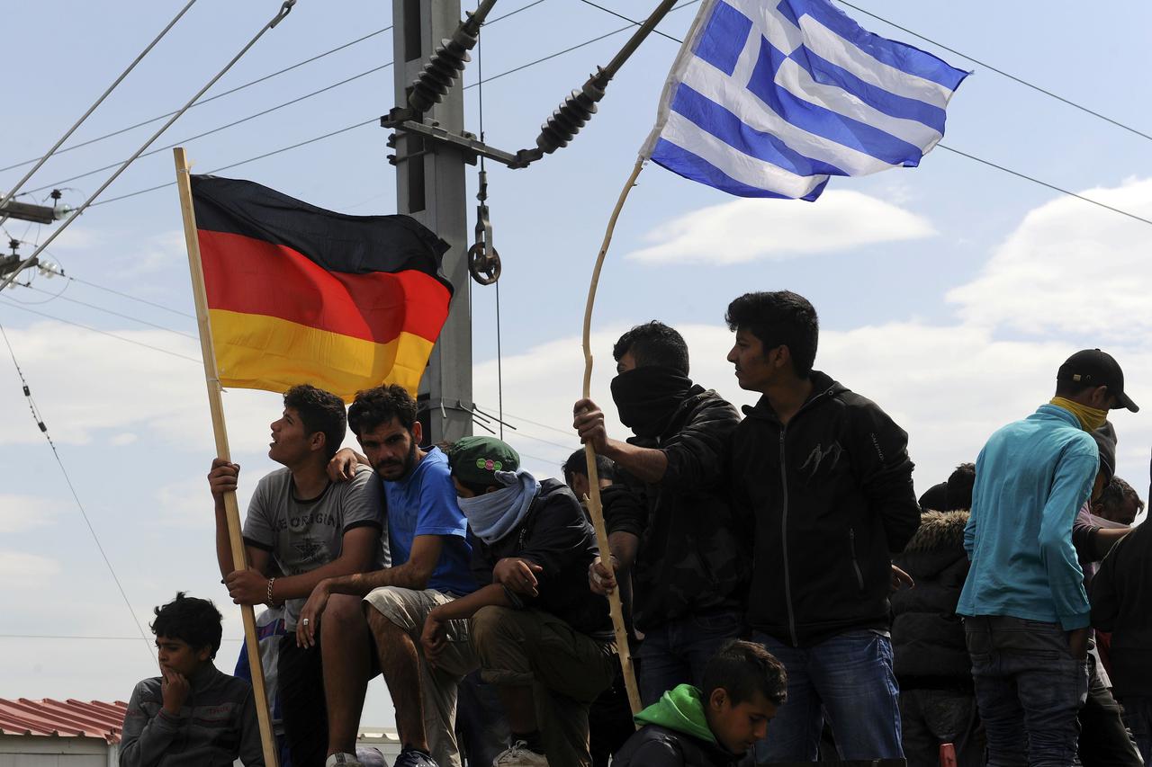 Migrants and refugees hold German and Greek flags as they sit on top of a train carriage at a makeshift camp at the Greek-Macedonian border near the village of Idomeni, Greece, April 11, 2016.  REUTERS/Alexandros Avramidis