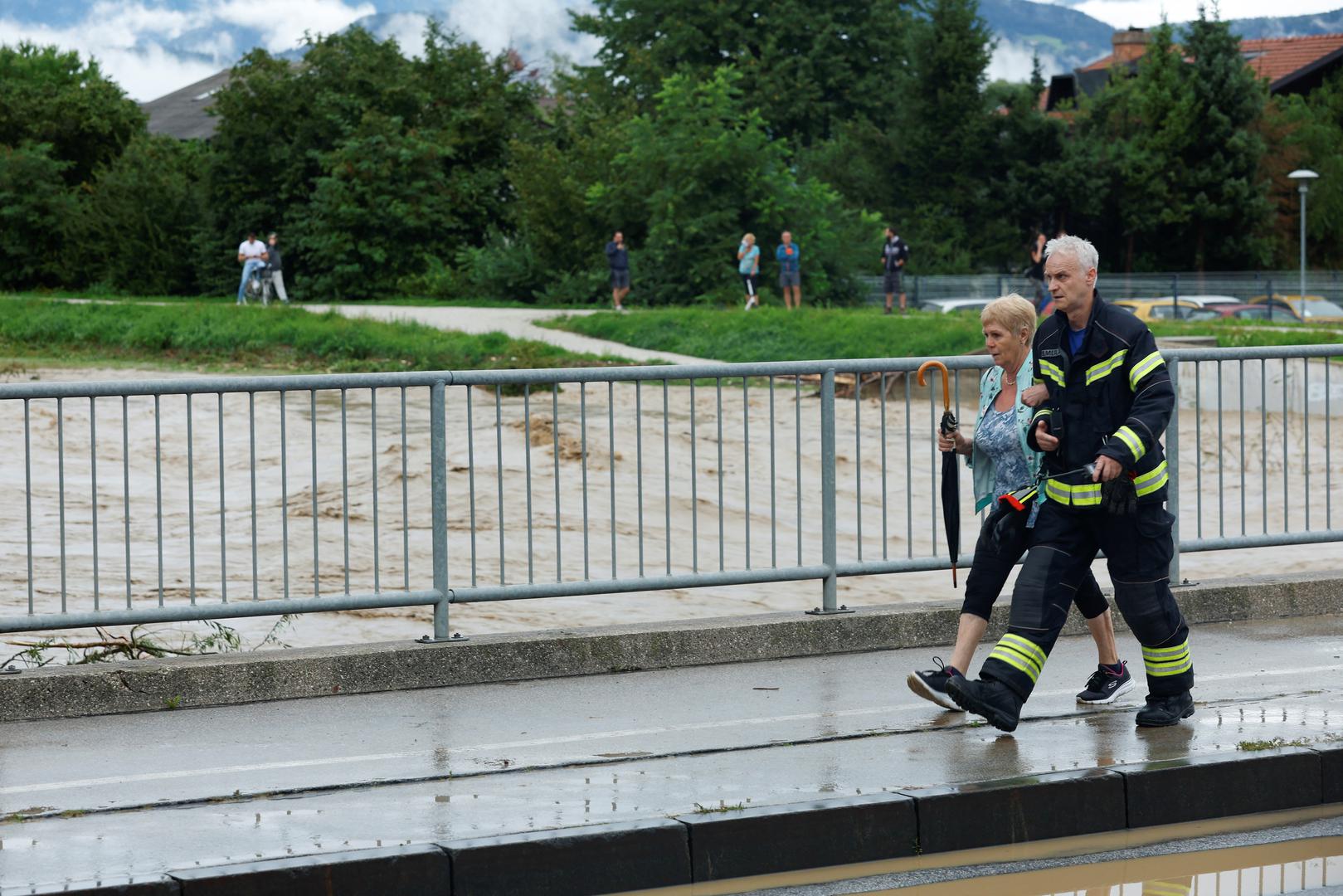 A firefighter helps a woman cross a closed bridge due to floods in Domzale, Slovenia August 4, 2023. REUTERS/Borut Zivulovic Photo: BORUT ZIVULOVIC/REUTERS