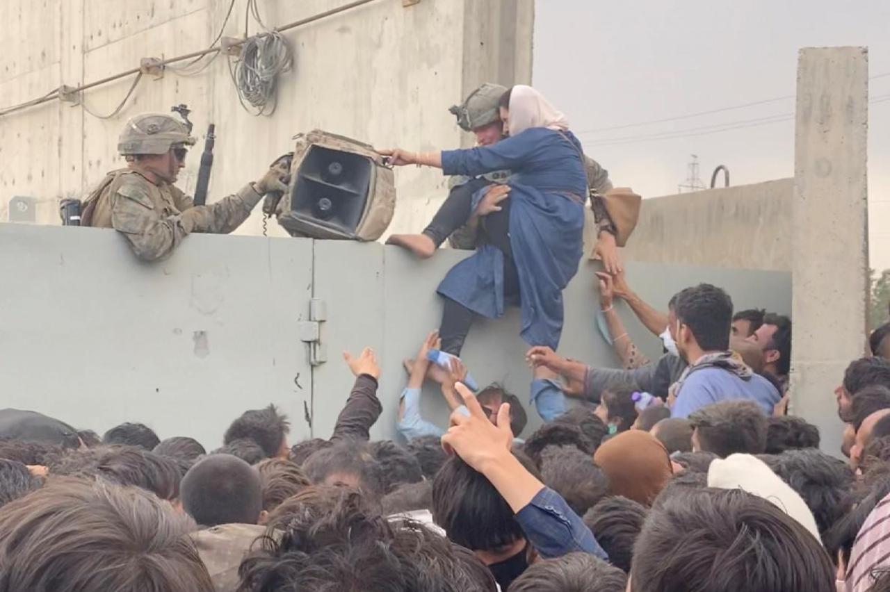 U.S. soldiers help a woman while she tries to climb over a fence as crowds gather near the wall at Kabul airport