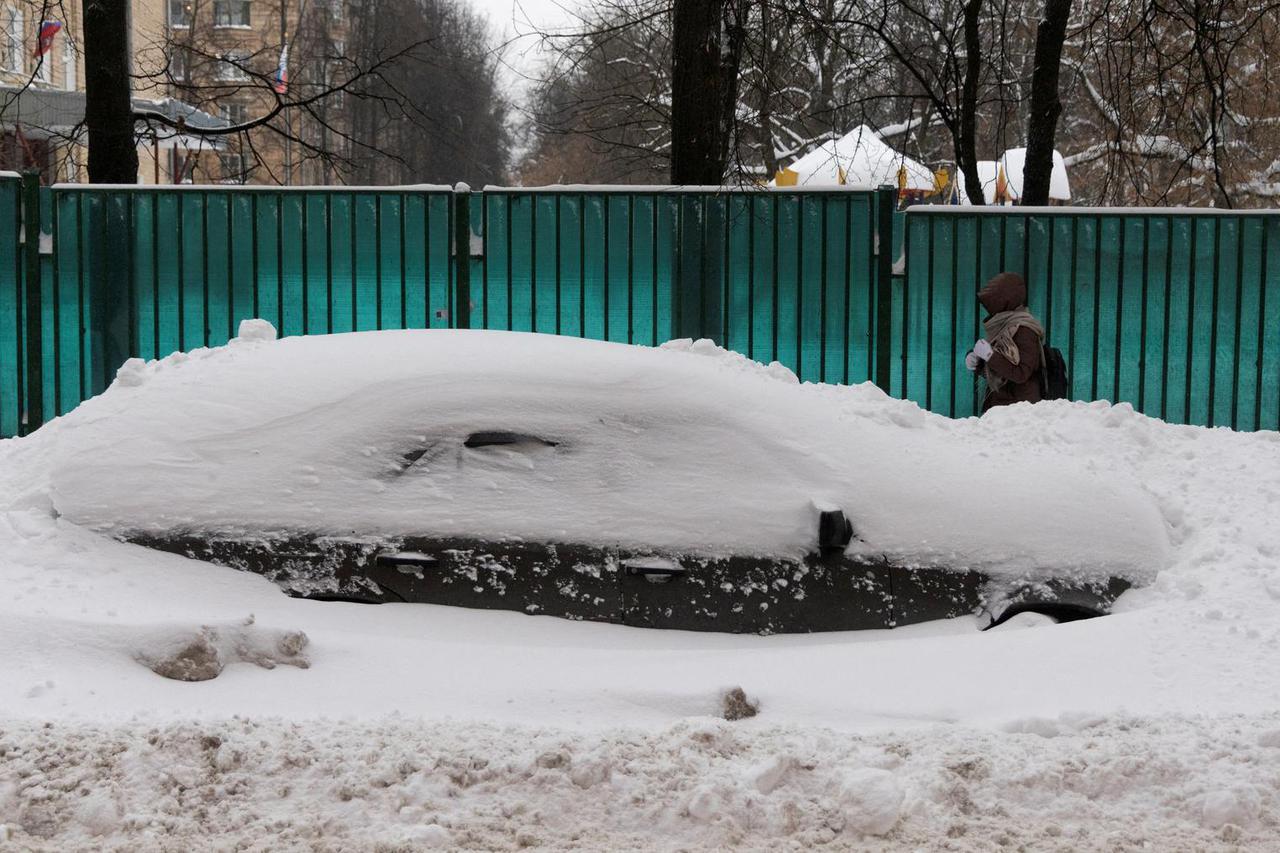 A woman walks past a car covered with snow after heavy snowfall in Moscow