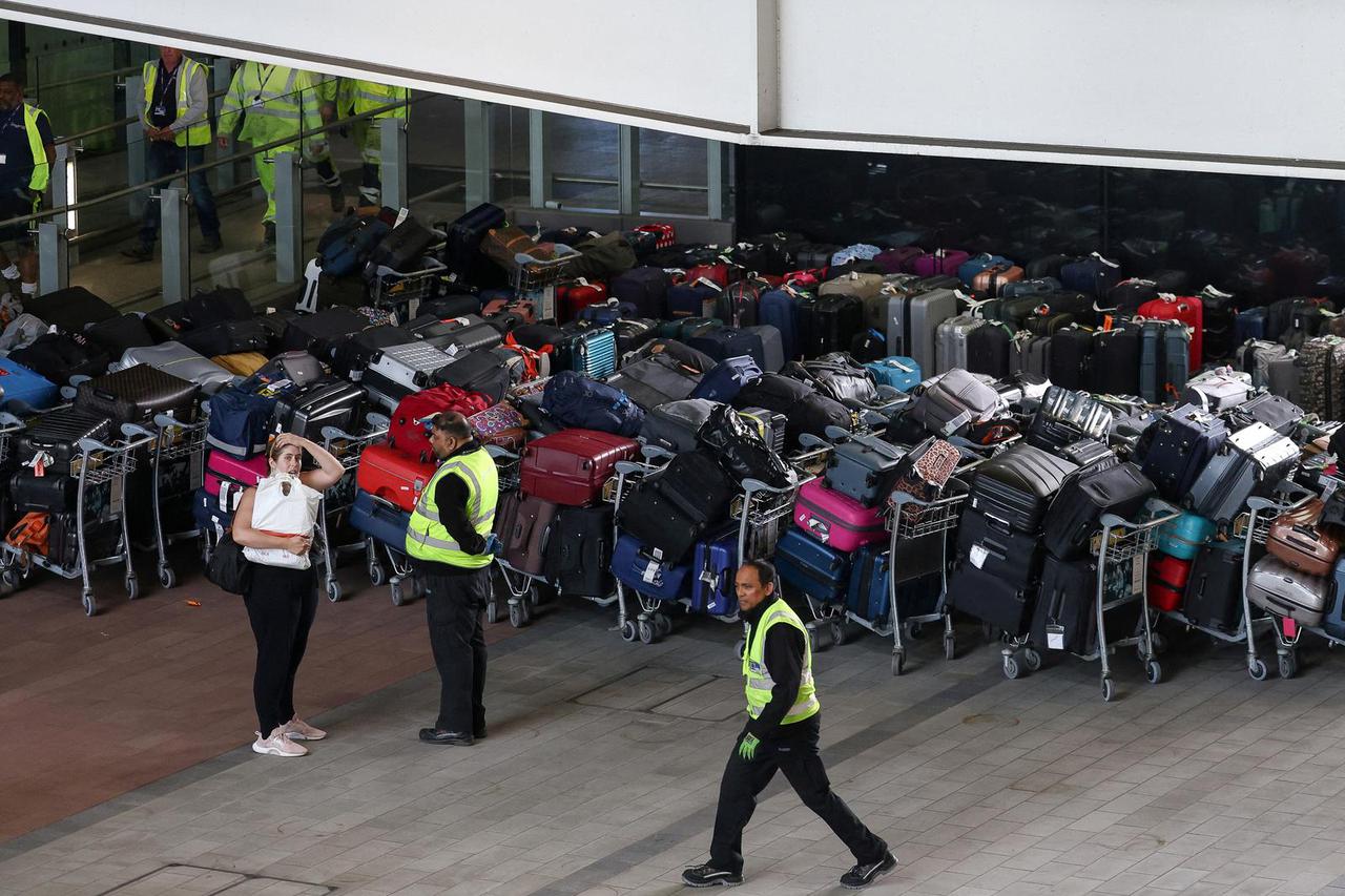 FILE PHOTO: Airport workers stand next to lines of passenger luggage arranged outside Terminal 2 at Heathrow Airport in London