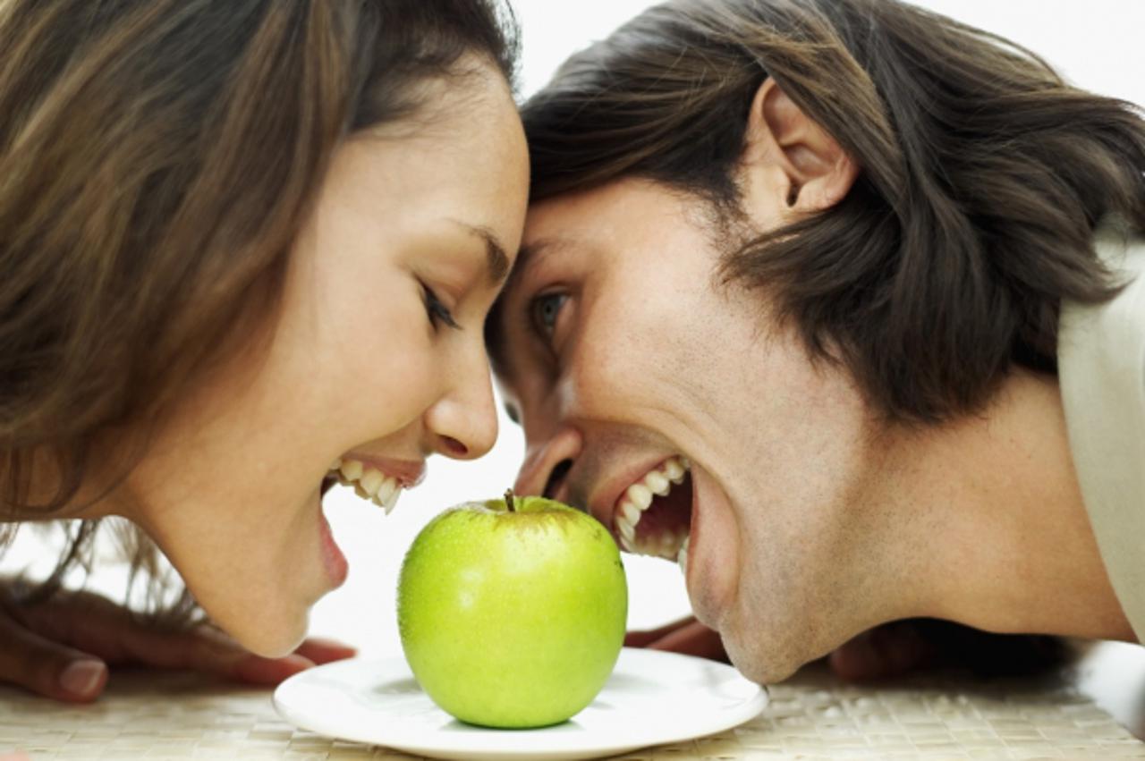 'close-up of a young couple trying to bite a green apple'