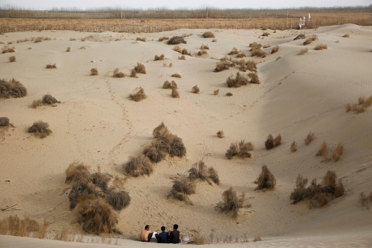 FILE PHOTO: Men sit at the foot of a dune in Taklamakan Desert outside the village of Jiya