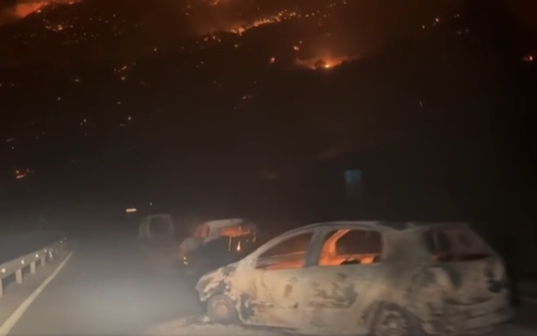 Cijelo područje obavijeno je gustim dimom, a nebo je osvijetljeno narančastim odsjajem vatre. Uz cestu su izgorjela i druga vozila, uključujući kombije i kamione.