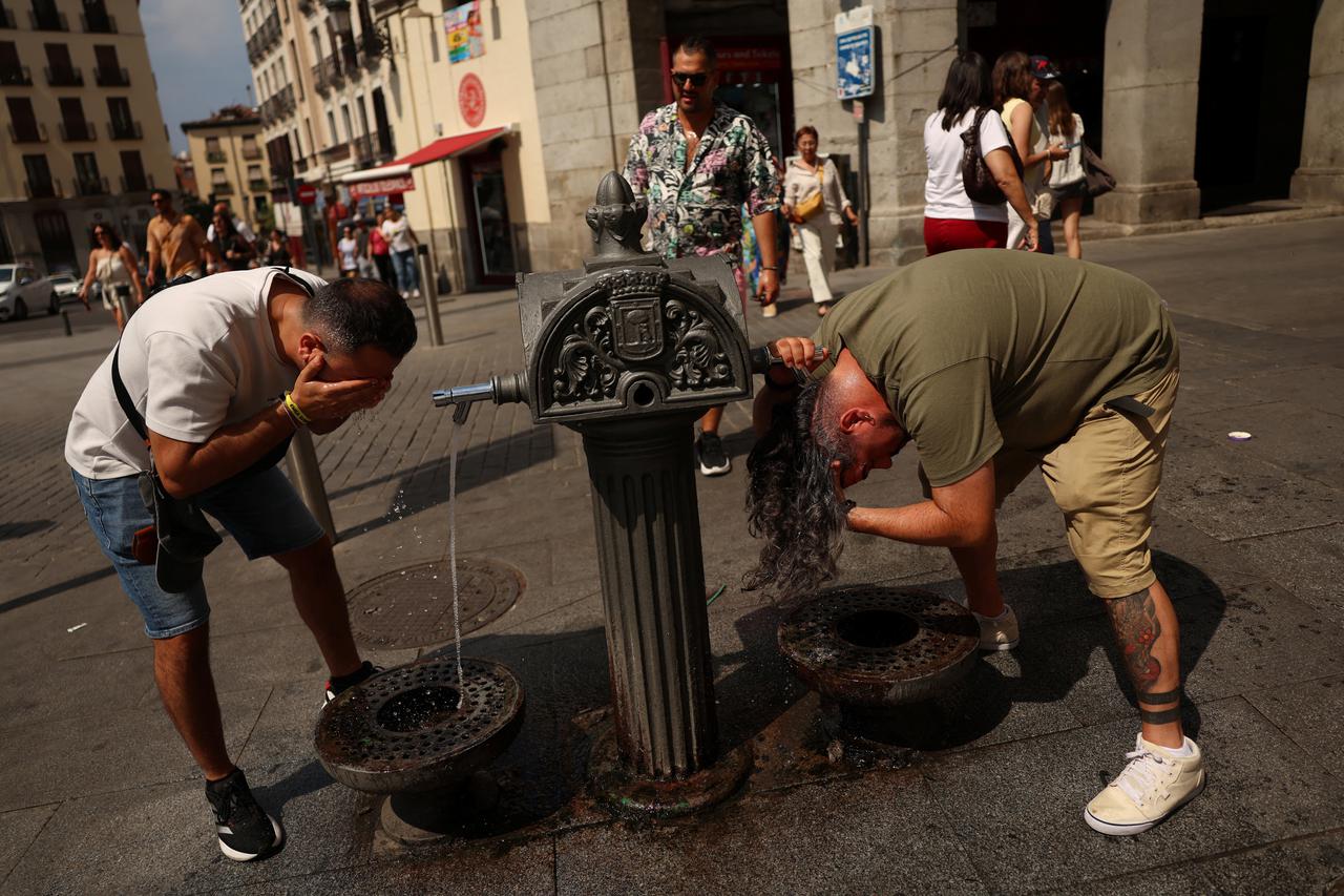 Men cool off at a water fountain during a heatwave in Madrid