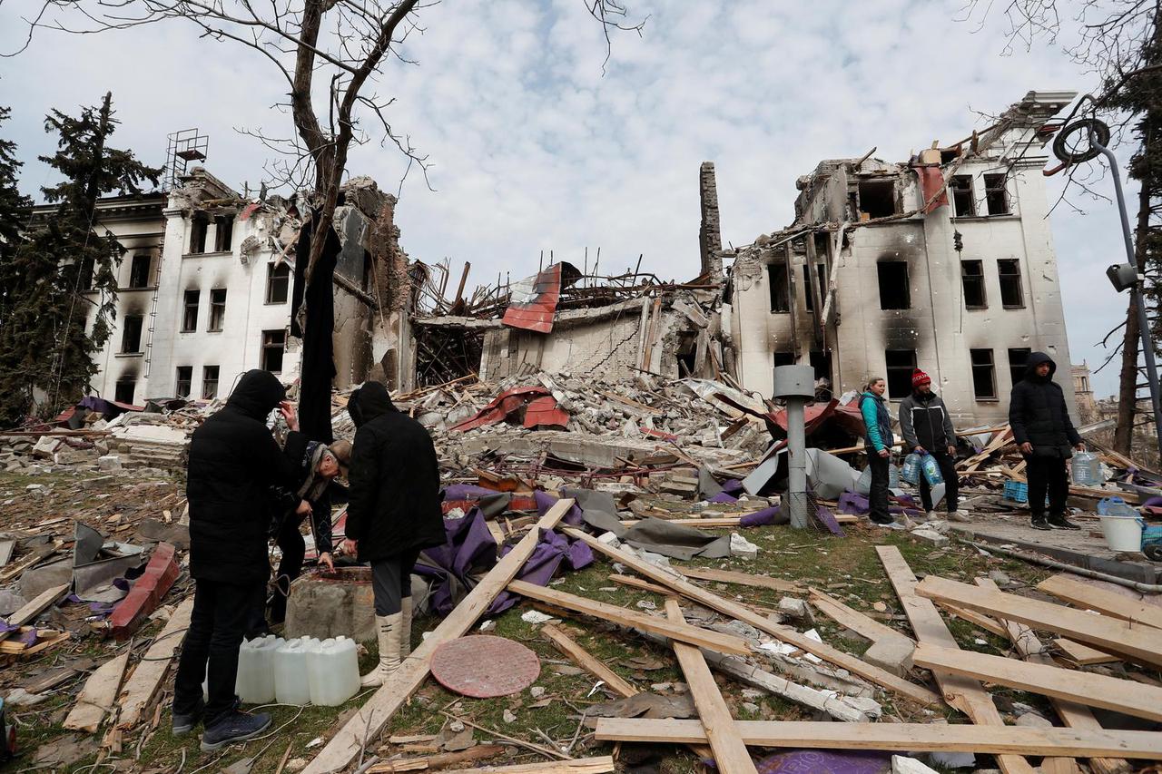 Local residents draw water from a well near the building of a destroyed theatre in Mariupol