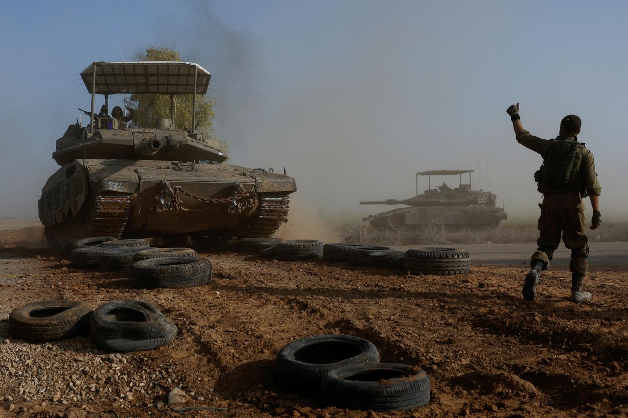 An Israeli soldier gestures towards a tank crew member as it crosses a road, as part of the convoy, amid the ongoing conflict between Israel and the Palestinian Islamist group Hamas, near Israel's border with southern Gaza, in Israel
