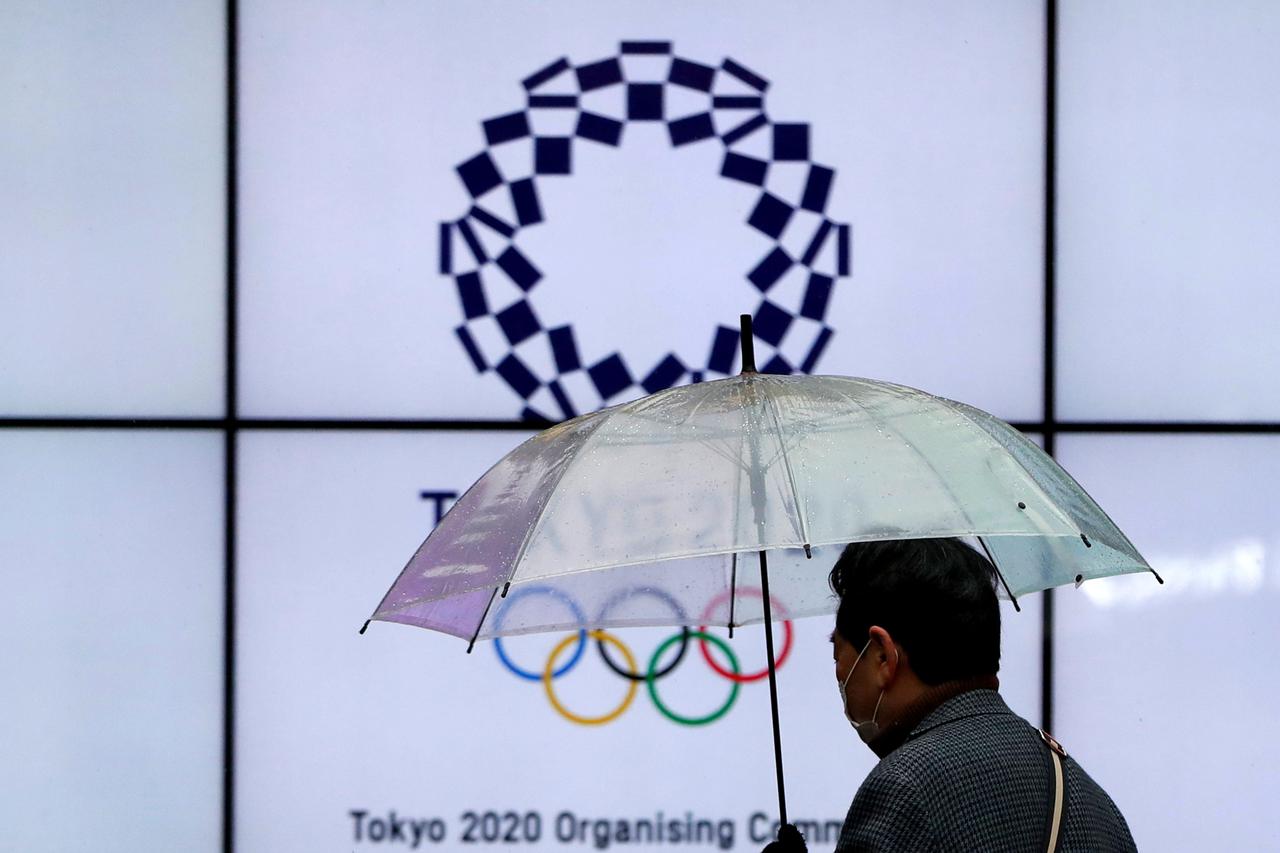FILE PHOTO: A man wearing a protective face mask walks past in front of a display showing the logo of Tokyo 2020 Olympic Games, amid the coronavirus disease (COVID-19) outbreak in Tokyo