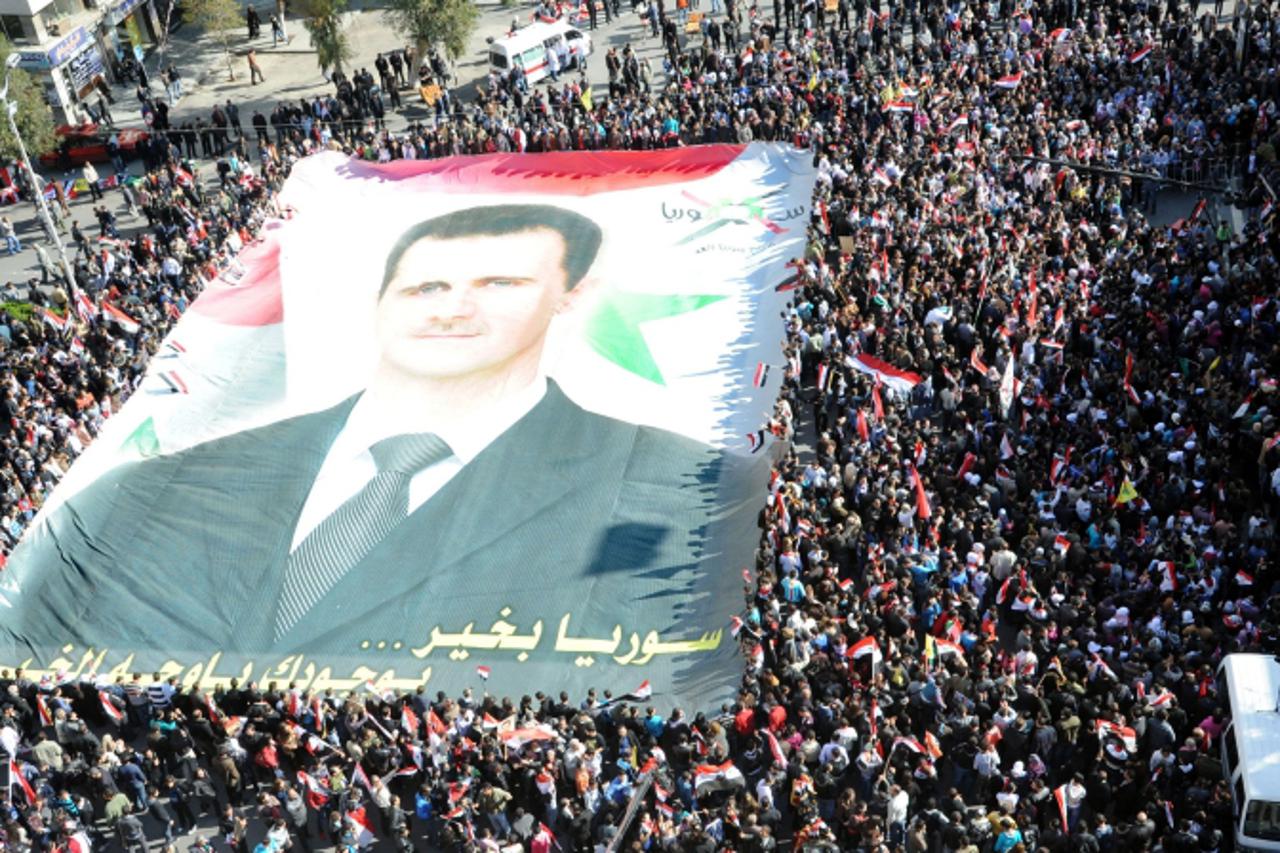 \'Syrians wave their national flag and hold up a huge banner of Syrian President Bashar al-Assad as they rally in central in Damascus on November 20, 2011, to show their support  as he defiantly vowed
