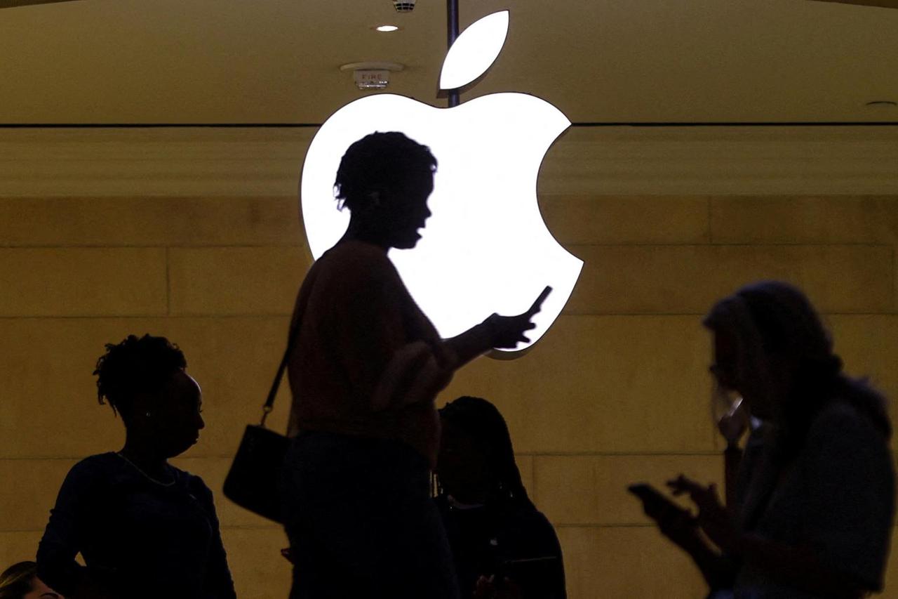 FILE PHOTO: women uses her iPhone mobile device as she passes a lighted Apple logo at the Apple store in New York
