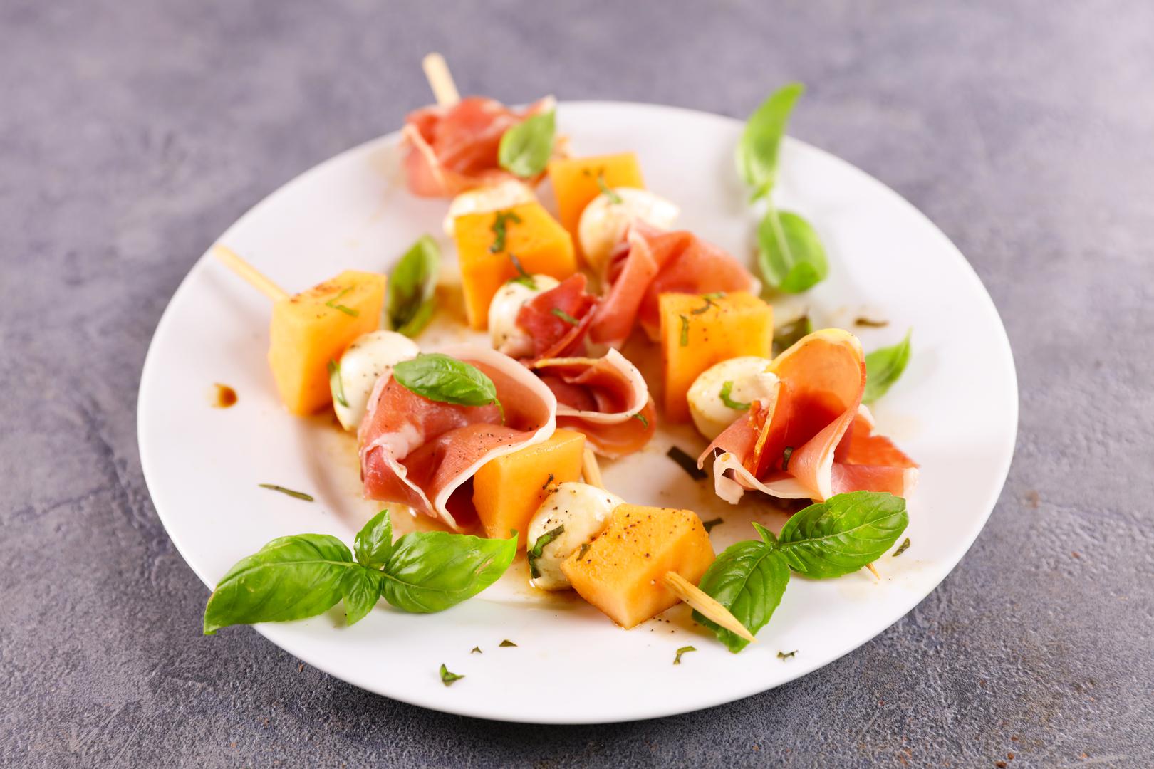 Ražnjići od pršuta i dinje: Ako još niste probali kombinaciju okusa pršuta i dinje, vrijeme je da to promijenite. Ova slatko-slana kombinacija idealna je kao ljetna užina jer će vas i zasititi i osvježiti. Na štapić za ražnjiće složite komadić dinje, bosiljak, mozzarellu, pršut i drugi komadić dinje i prelijte ražnjiće balzamičnim octom.