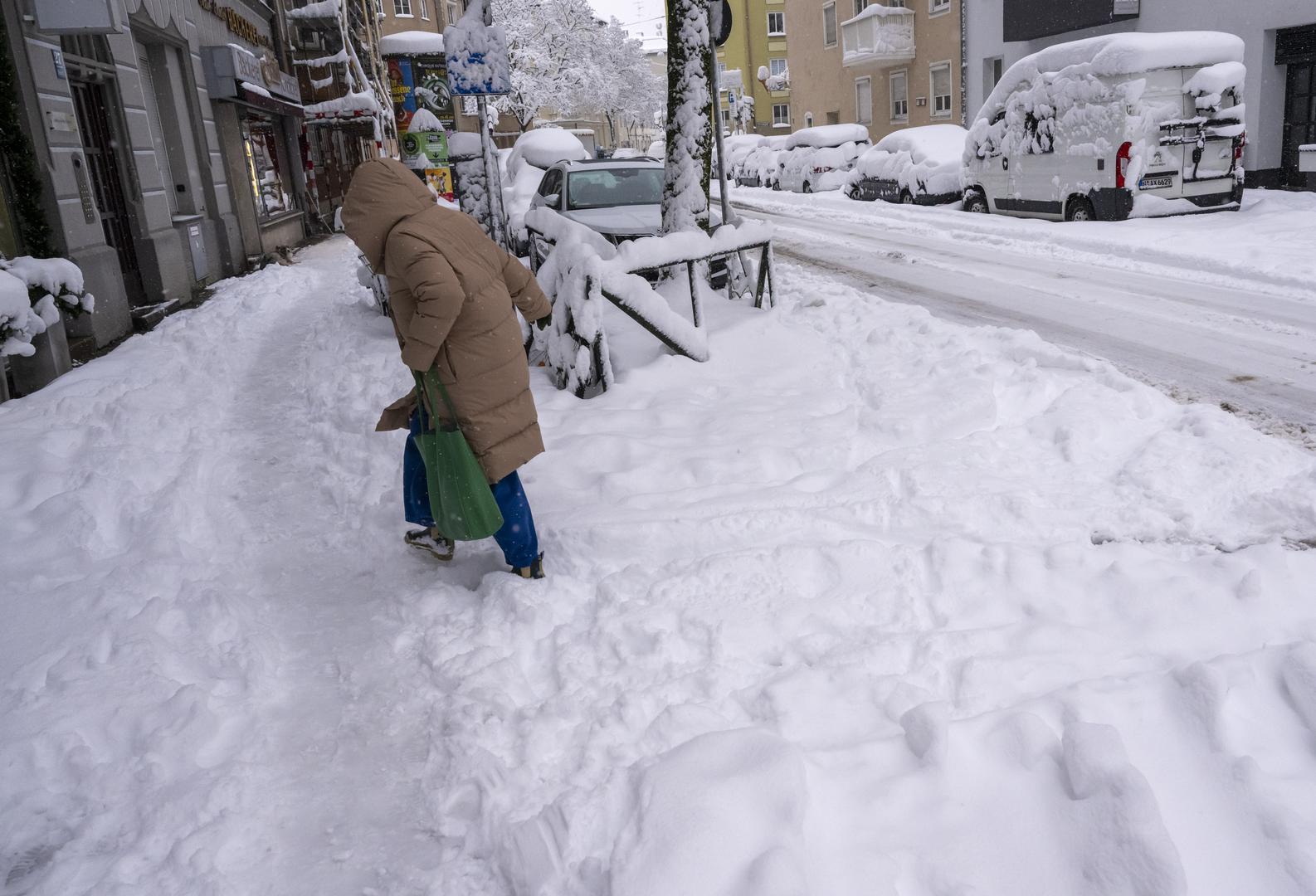 02 December 2023, Bavaria, Munich: A woman walks across a snow-covered street onto an equally snow-covered sidewalk. Snow and ice have caused chaos on the roads and on the railroads in southern Bavaria. Photo: Peter Kneffel/dpa Photo: Peter Kneffel/DPA