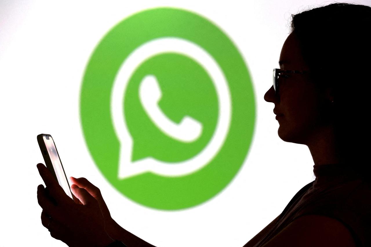 FILE PHOTO: Illustration shows a teenager posing for a photo while holding a smartphone in front of a Whatsapp logo