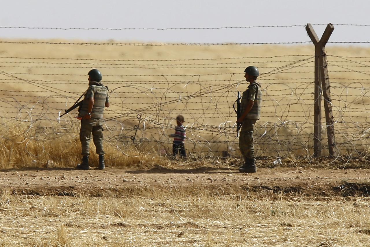 Turkish soldiers stand guard as a Syrian refugee boy waits behind the border fences to cross into Turkey on the Turkish-Syrian border, near the southeastern town of Akcakale in Sanliurfa province, Turkey, June 5, 2015. To match Special Report EUROPE-MIGRA