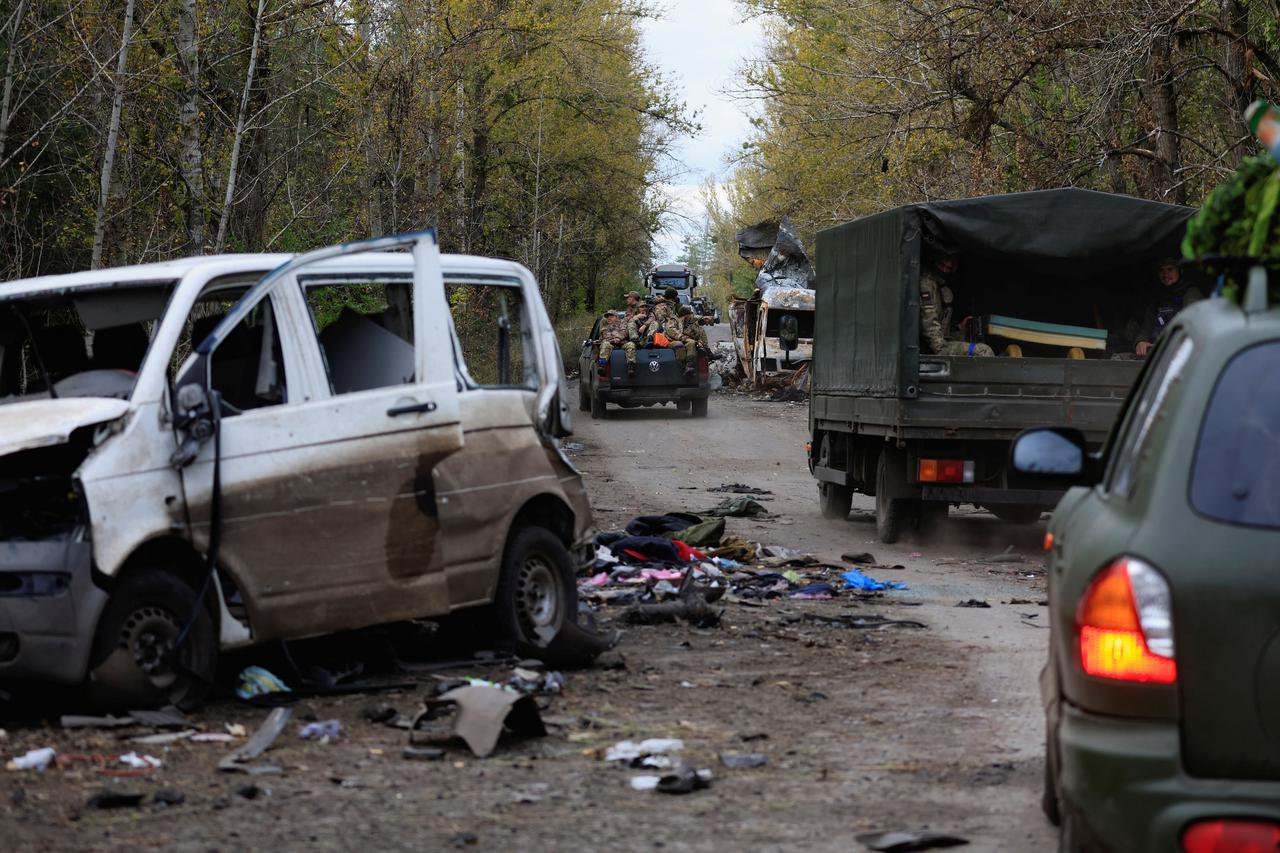 Ukrainian army soldiers drive past a blasted white van in which, according to Ukrainian military officers, last weekend a Russian army unit was speeding in retreat toward the eastern town of Lyman,outside the recently liberated town of Lyman,