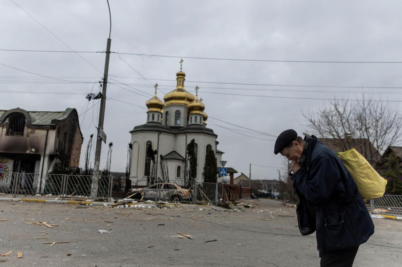 A man takes a pause as he evacuates from the town, on the only escape route used by locals after days of heavy shelling, while Russian troops advance towards the capital, in Irpin, near Kyiv