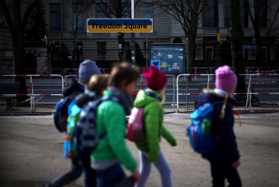 Children walk past a sign reading 'Freedom Square' in the national colours of Ukraine in front of the Russian embassy in Berlin