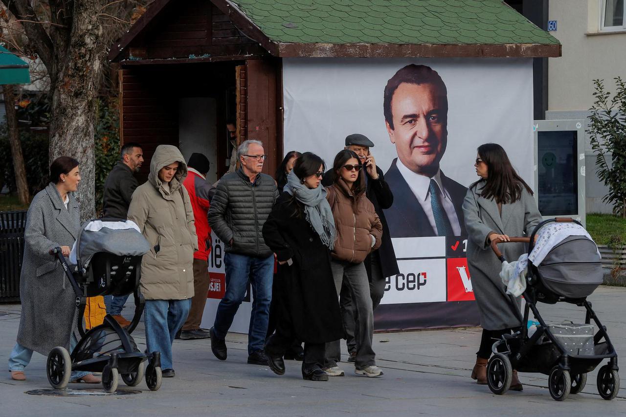 FILE PHOTO: Pedestrians walk near a campaign poster for the upcoming parliamentary elections, in Pristina