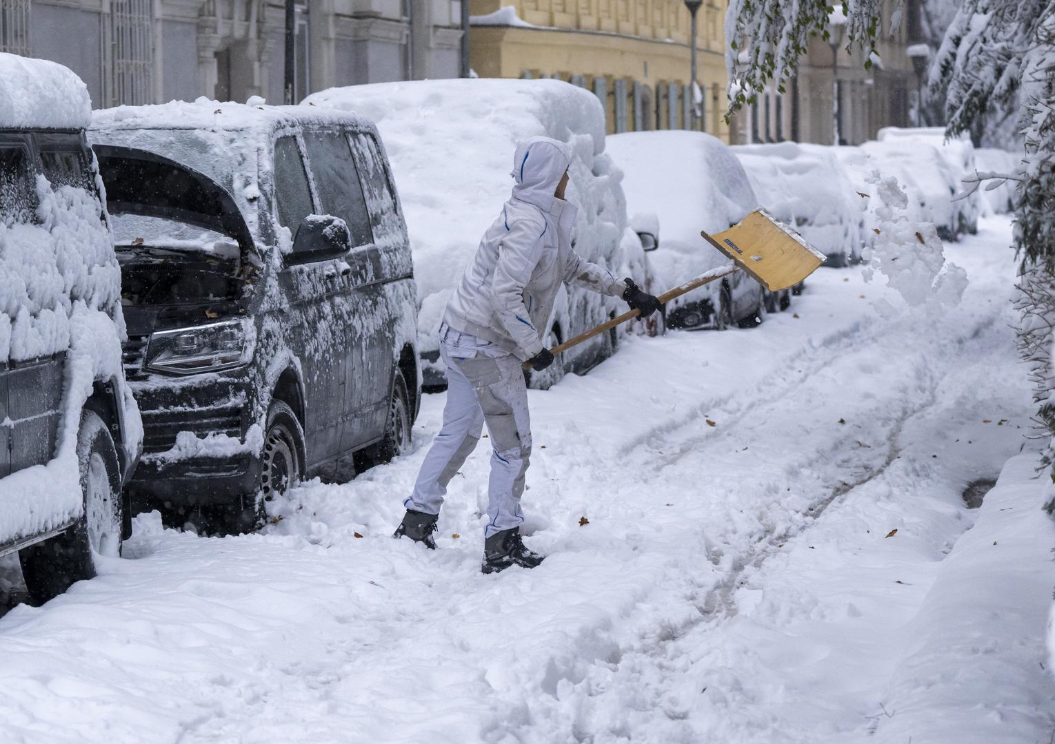 02 December 2023, Bavaria, Munich: A woman shovels snow next to her snow-covered parked car. Snow and ice have caused chaos on the roads and on the railroads in southern Bavaria. Photo: Peter Kneffel/dpa Photo: Peter Kneffel/DPA
