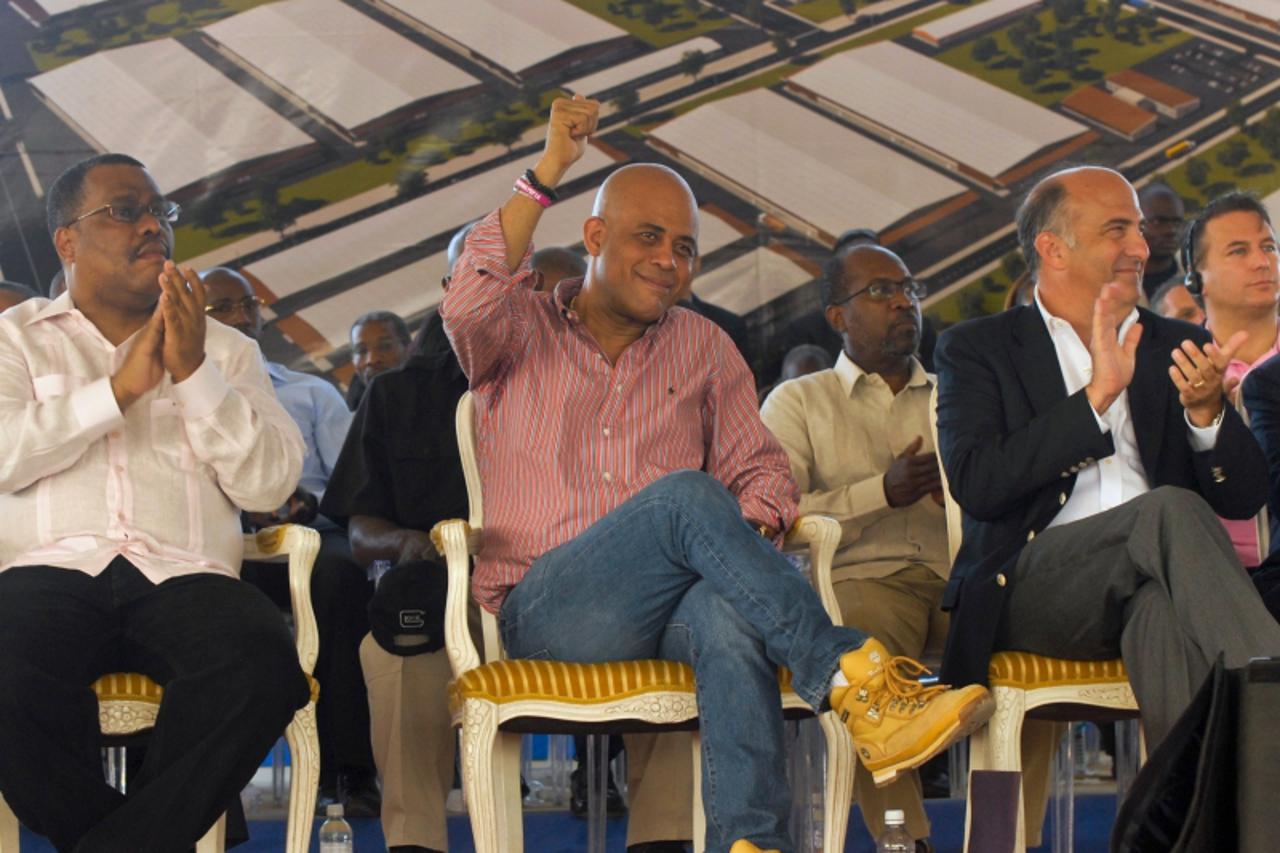 \'Haitian President Michel Martelly (C), sitting between Haitian Prime Minister Garry Conille (L) and U.S. Ambassador to Haiti, Kenneth H. Merten (2nd R), gestures to the crowd while attending a news 