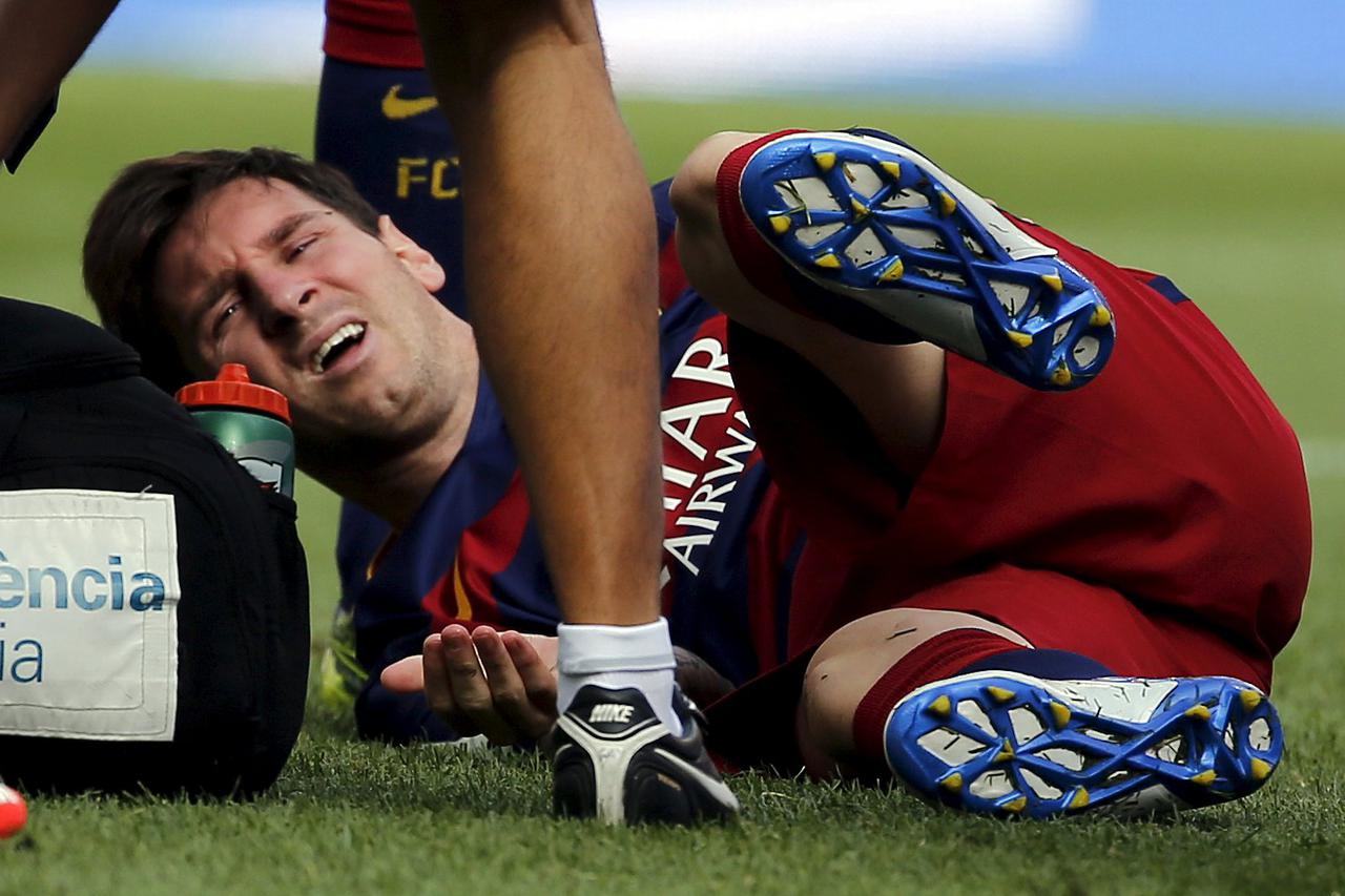 Barcelona's Lionel Messi grimaces as he lies on the pitch after injuring his left knee during their Spanish first division soccer match against Las Palmas at Camp Nou stadium in Barcelona, Spain, September 26, 2015. REUTERS/Sergio Perez