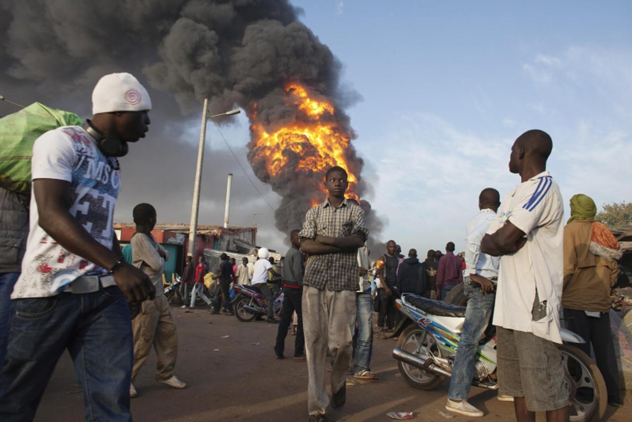 'Onlookers walk past a fire at Ngolonina market in the Malian capital of Bamako, January 12, 2013. The fire was started after an accident at a gasoline depot. REUTERS/Joe Penny (MALI - Tags: DISASTER 