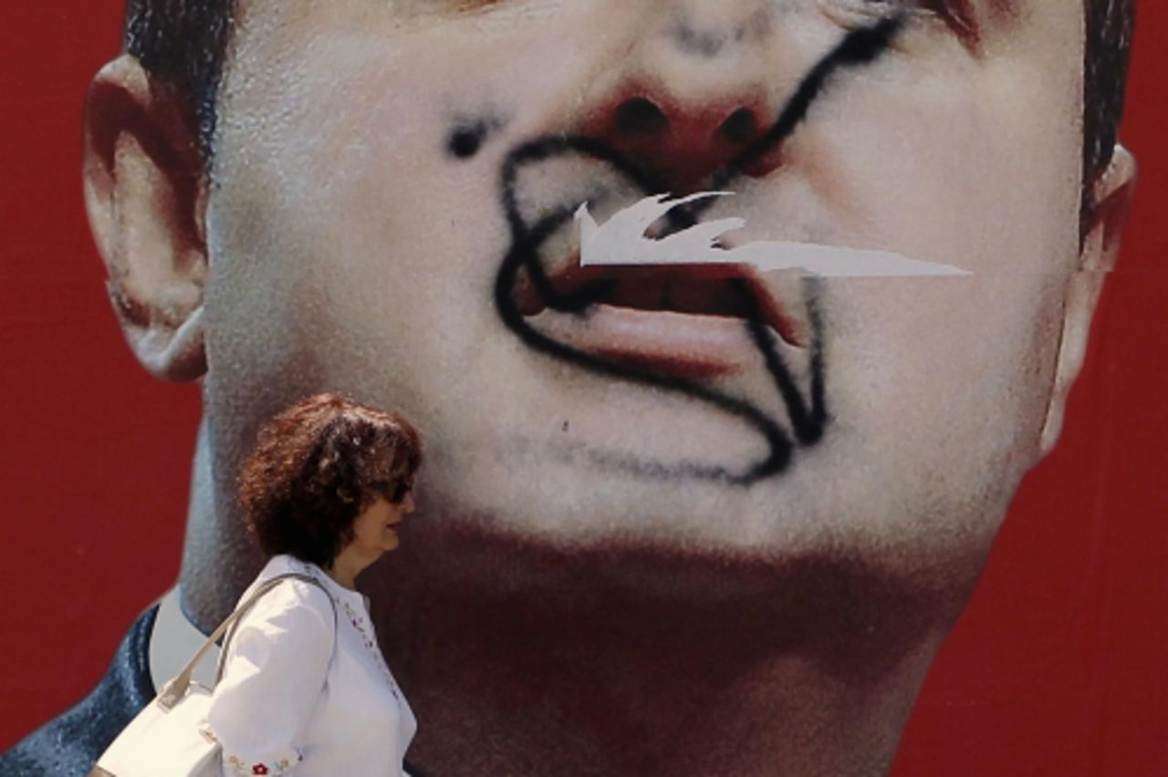'A woman passes a defaced pre-election billboard of the Socialist party leader Ivica Dacic in Belgrade May 7, 2012. The Socialist Party of late strongman Slobodan Milosevic held the key to power in Se