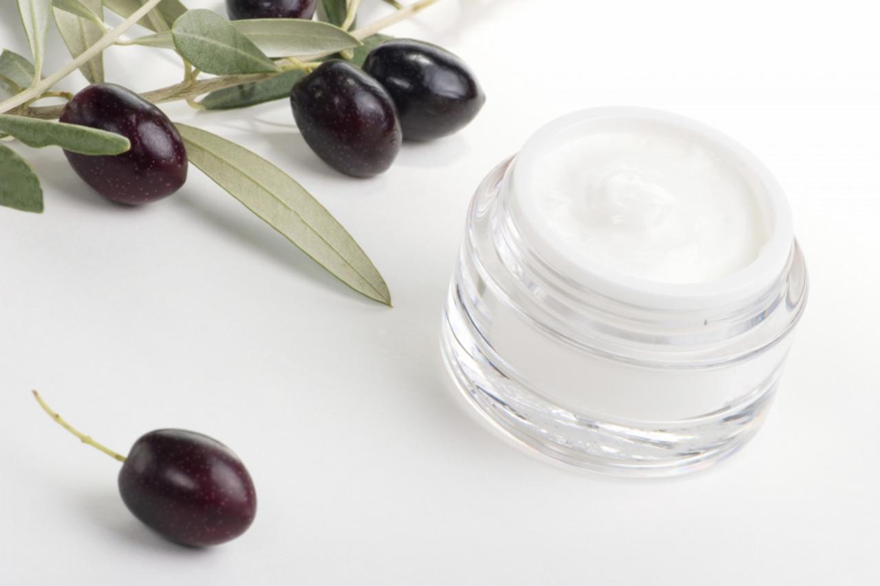 'Closeup of jar of moisturizing face cream and twig with black olives.'