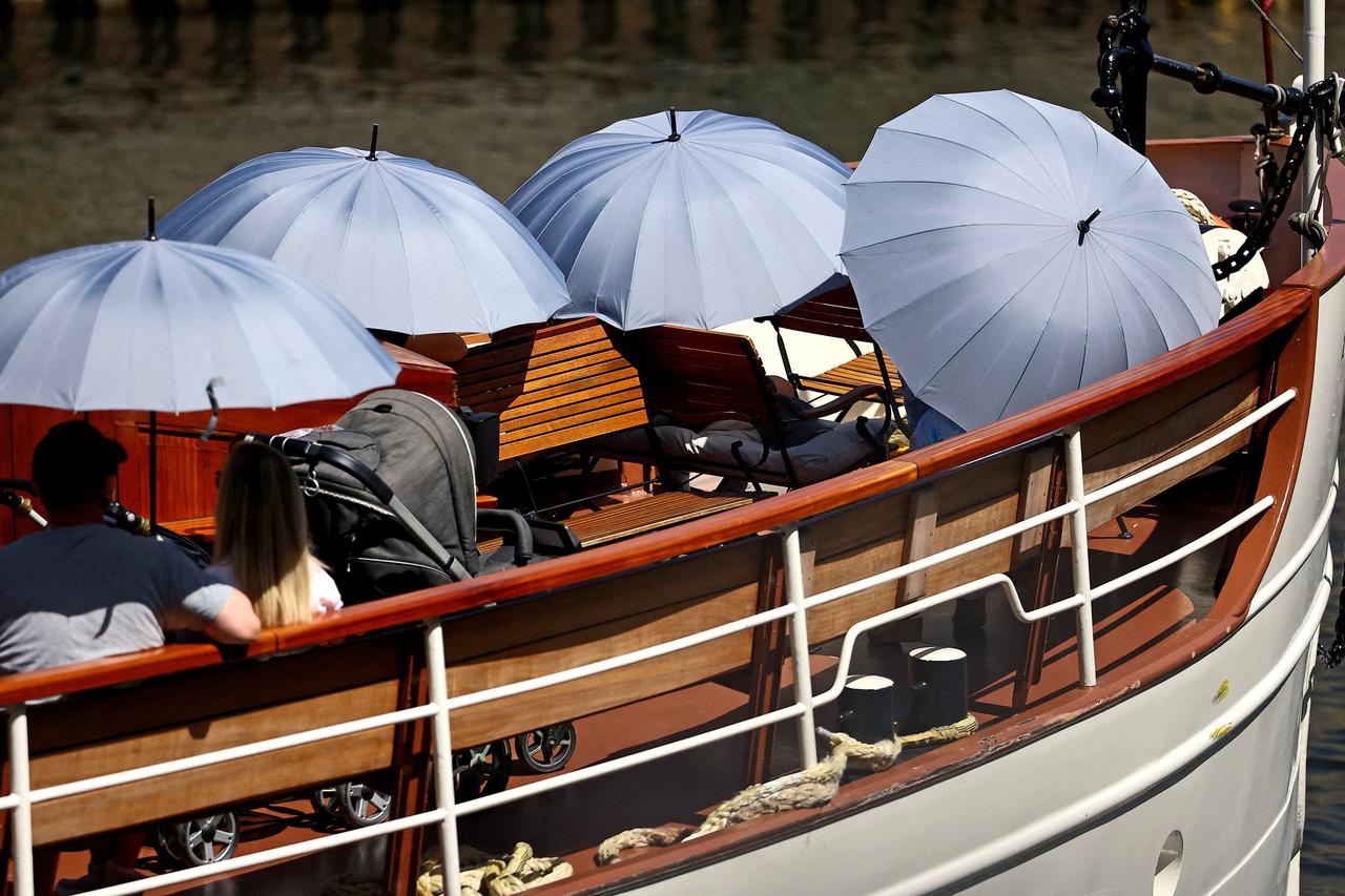 People use umbrellas to shelter from sun as they take a boat ride in Berlin