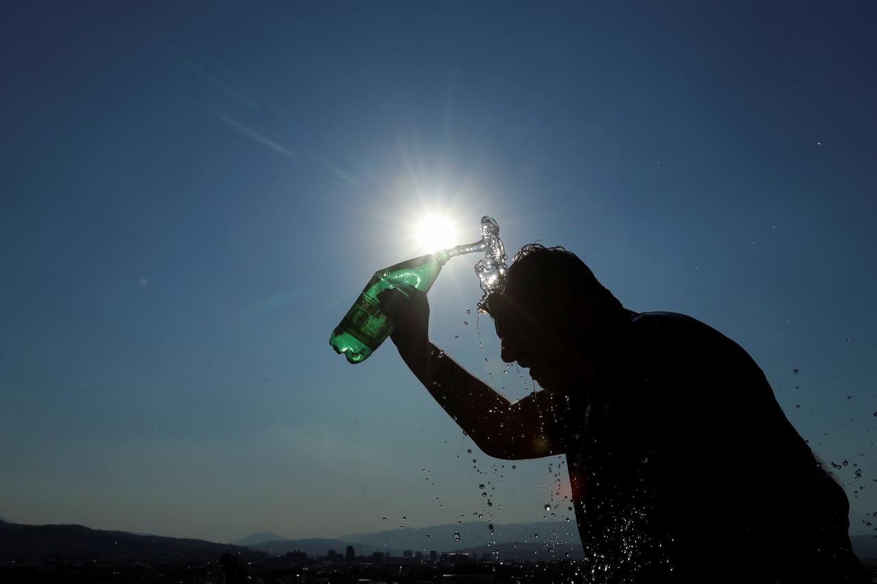 Victor, a tourist guide, pours water from a bottle to cool off during hot weather in Skopje