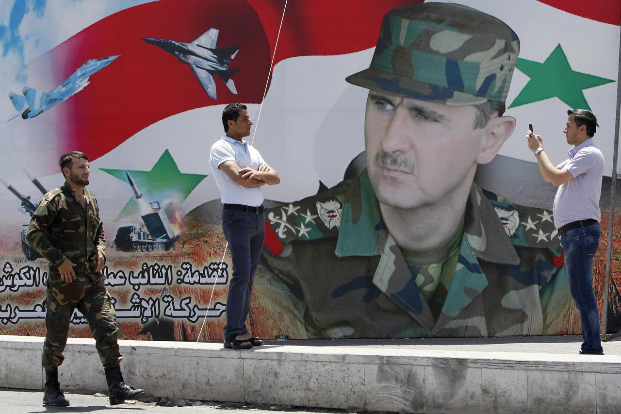 A man takes a photo of his friend in front of a poster of Syria's President Bashar al-Assad at Umayyad Square in Damascus May 16, 2014. Syria is holding a presidential election for June 3, preparing the ground for Assad to defy widespread opposition and e