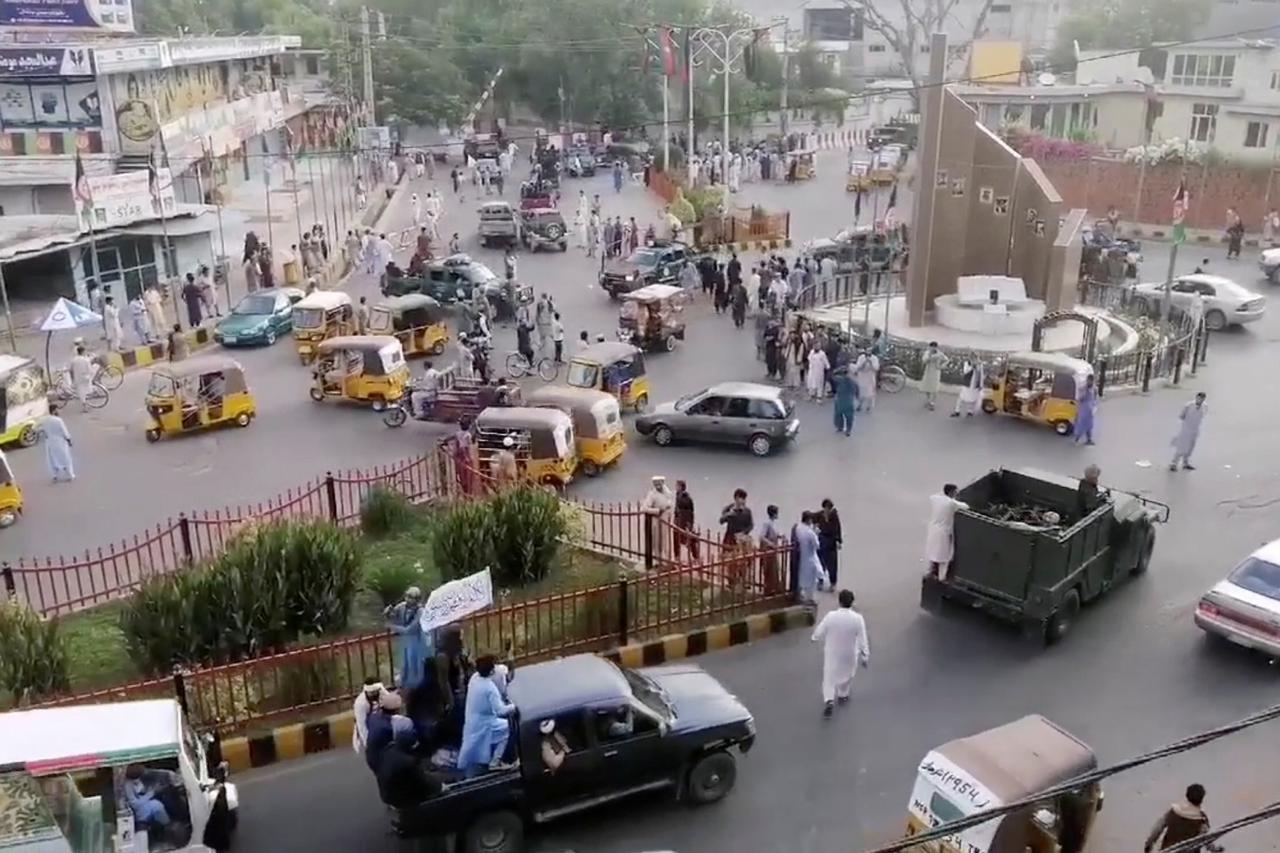 Taliban militants drive past a crowded street at Pashtunistan Square area in Jalalabad