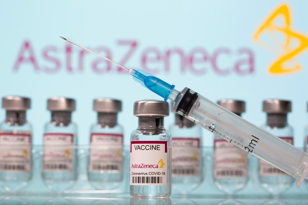 Vials labelled "AstraZeneca COVID-19 Coronavirus Vaccine" and a syringe are seen in front of a displayed AstraZeneca logo