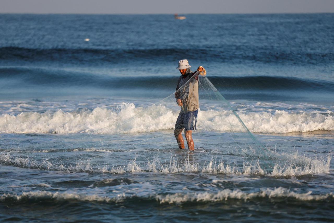 Palestinian fisherman throws his net on the beach as he prepares it for fishing in Khan Younis
