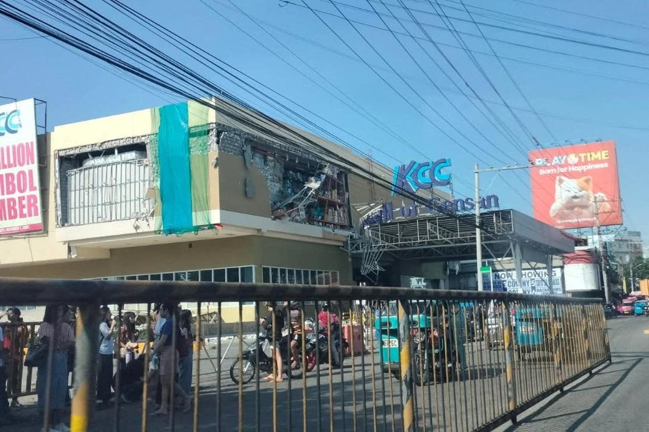People stand near a damaged building after an earthquake, in General Santos City