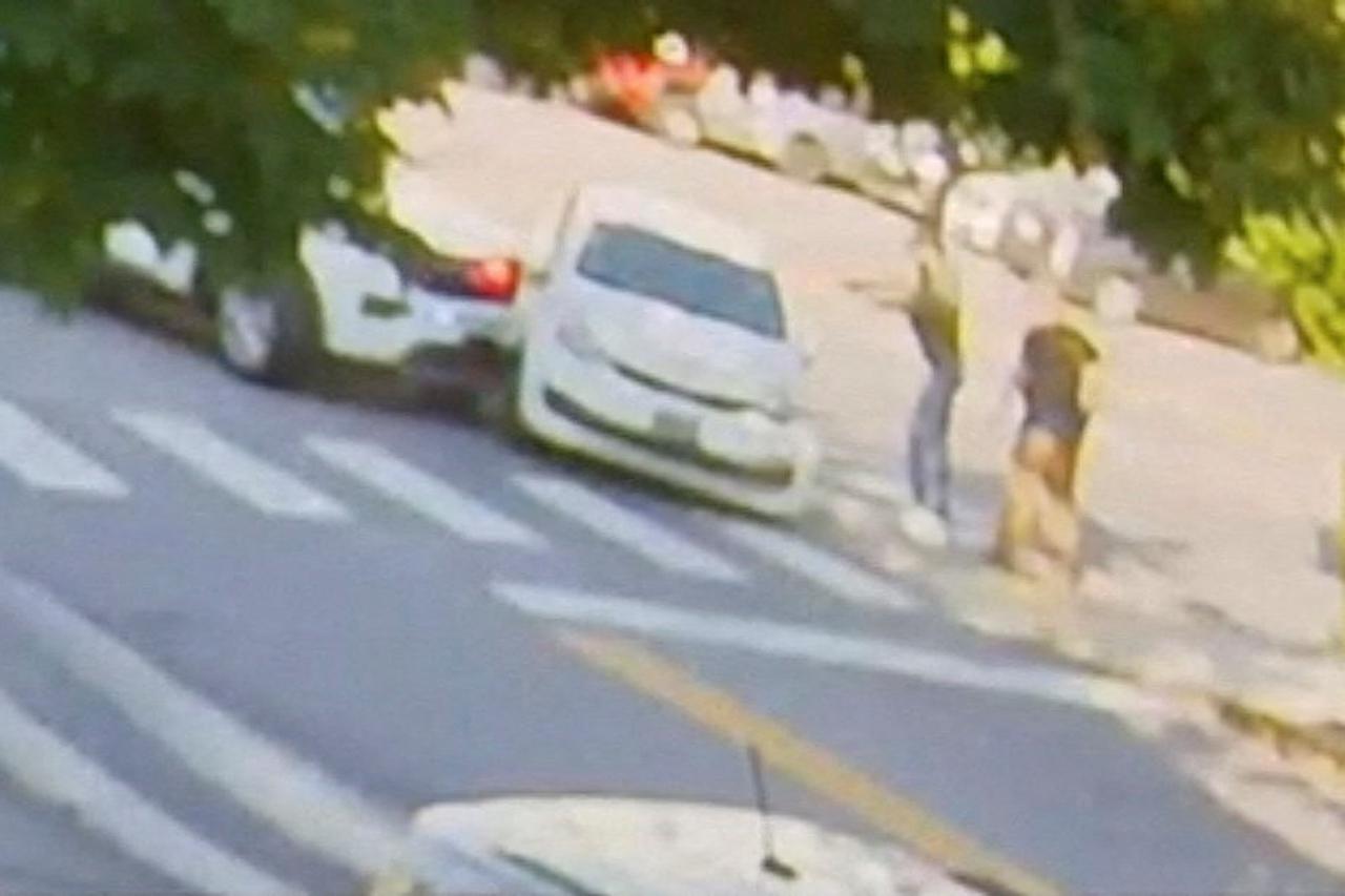 A person believed to be a U.S. Immigration and Customs Enforcement officer holds out his hands towards the driver's side of a vehicle in Biddeford