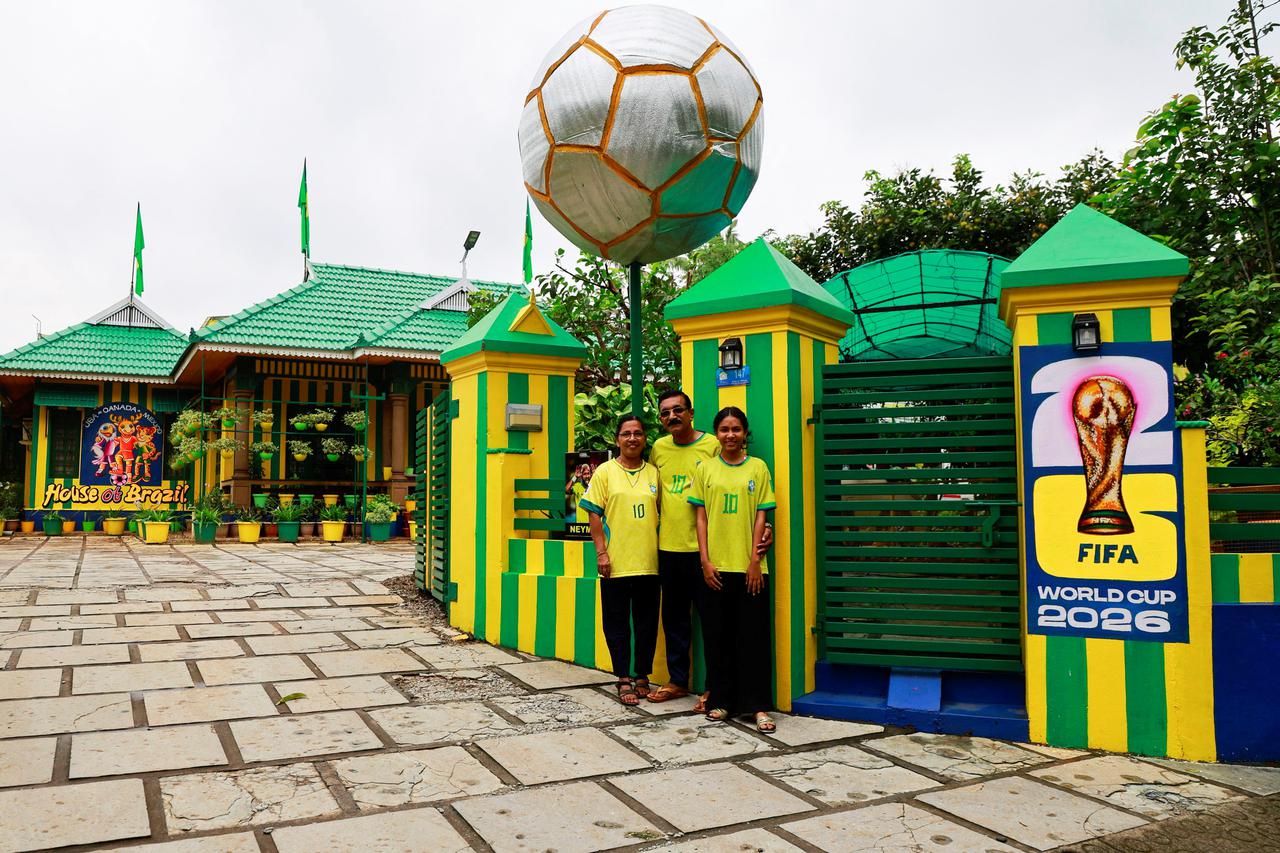 Salu Paul, a fan of Brazilian soccer team poses with his wife Lathi, and daughter Nayana in front of their house painted with the Brazilian national colours ahead of the 2026 FIFA World Cup, in Mekkad, Kerala