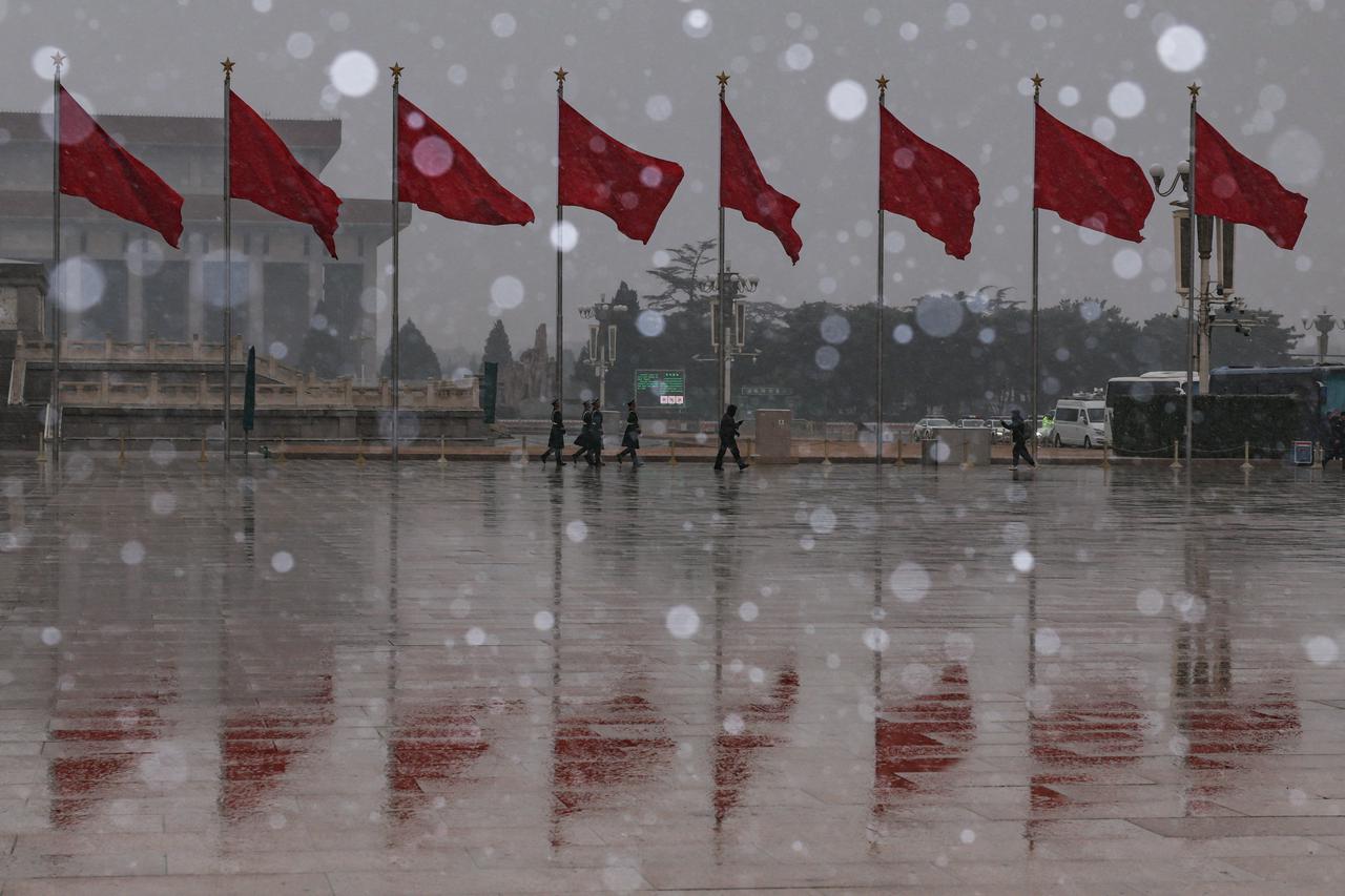 Paramilitary police officers march past flags fluttering at Tiananmen Square amid snowfall before the opening sessions of the annual CPPCC