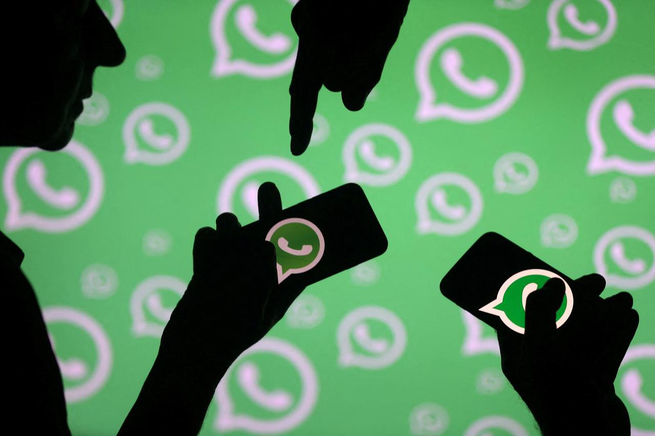 FILE PHOTO: Men pose with smartphones in front of displayed Whatsapp logo