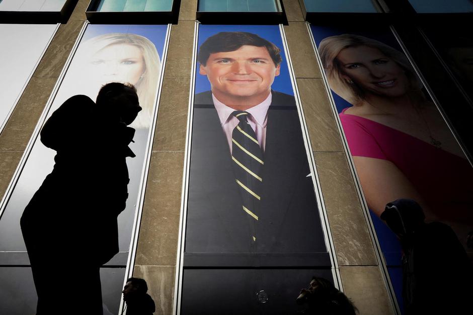 FILE PHOTO: People pass by a promo of Fox News host Tucker Carlson on the News Corporation building in New York