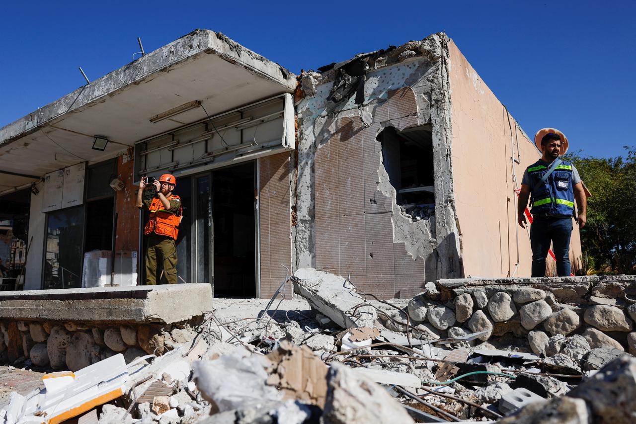 Men stand next to a damaged building that was hit by a rocket launched from the Gaza Strip, in Netivot