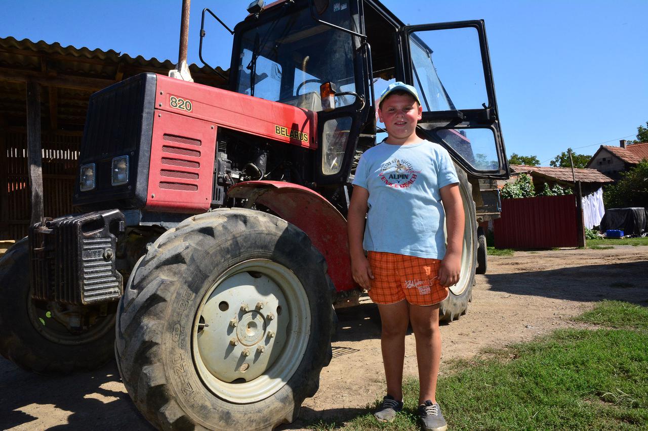 28.08.2015. Slavonski Brod - Toni OIujević (10) iz Bebrine pokraj Slavonskog Broda jedan je od najmladjih traktorista u Hrvatskoj. Snimljen u traktoru, kako hrani svinje i goveda, pomaze u poslovima silaze kukuruza...na fotkama i s ocem Stjepanom Photo: I
