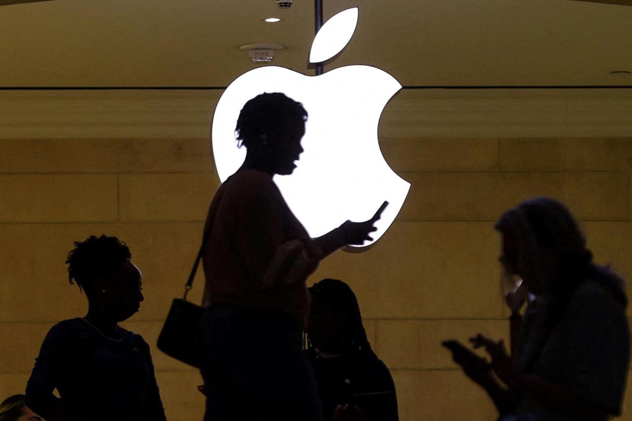 FILE PHOTO: women uses her iPhone mobile device as she passes a lighted Apple logo at the Apple store in New York