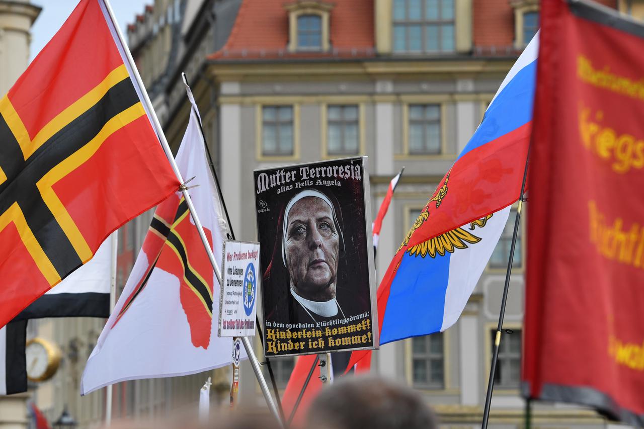 Supporters of the anti-islam, right-wing populist political movement 'Pegida' hold up flags like the Wirmer flag?(L) and a poster with the words 'Mutter Terroresia alias Hells Angela in the epochal Refugee drama: Kinderlein kommet (Children come!) (crosse