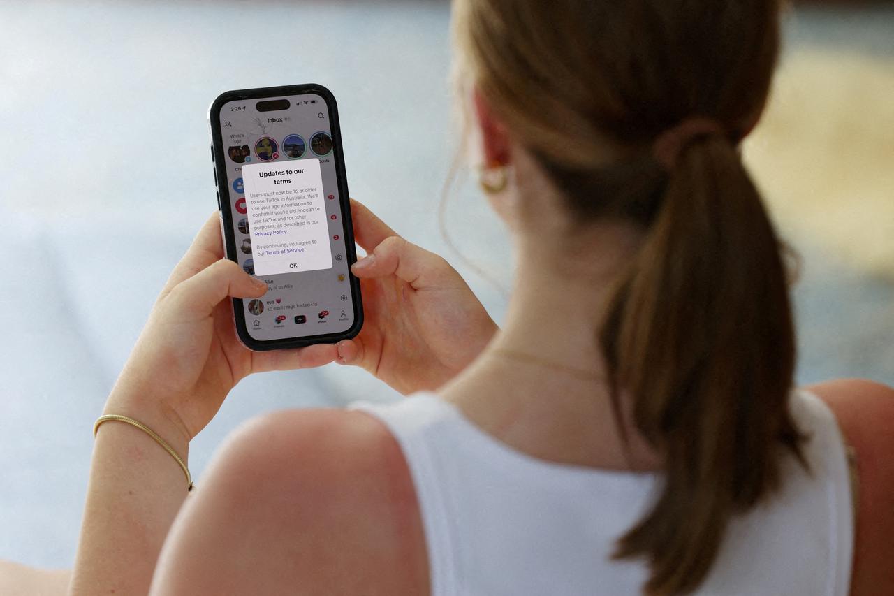 FILE PHOTO: A teenager poses holding a mobile phone displaying a message from TikTok in Sydney
