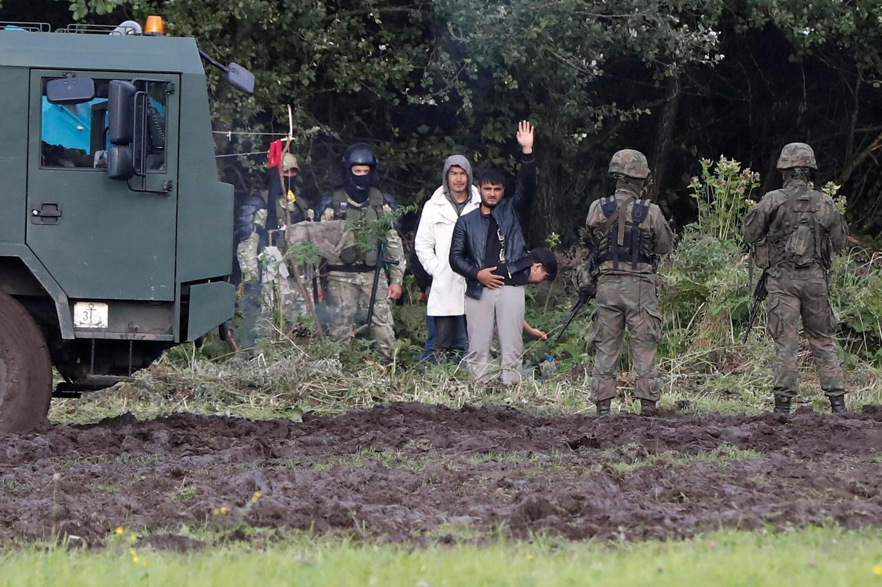 FILE PHOTO: Polish border guard officers stand next to a group of migrants stranded on the border between Belarus and Poland near the village of Usnarz Gorny