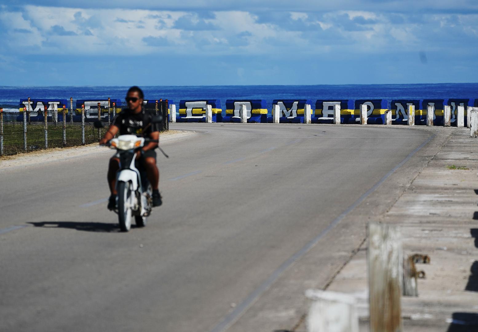 (240118) -- YAREN, Jan. 18, 2024 (Xinhua) -- A man rides a motorcycle on a road near the sea in the Republic of Nauru, Jan. 18, 2024. (Xinhua/Wang Shen) Photo: Wang Shen/XINHUA