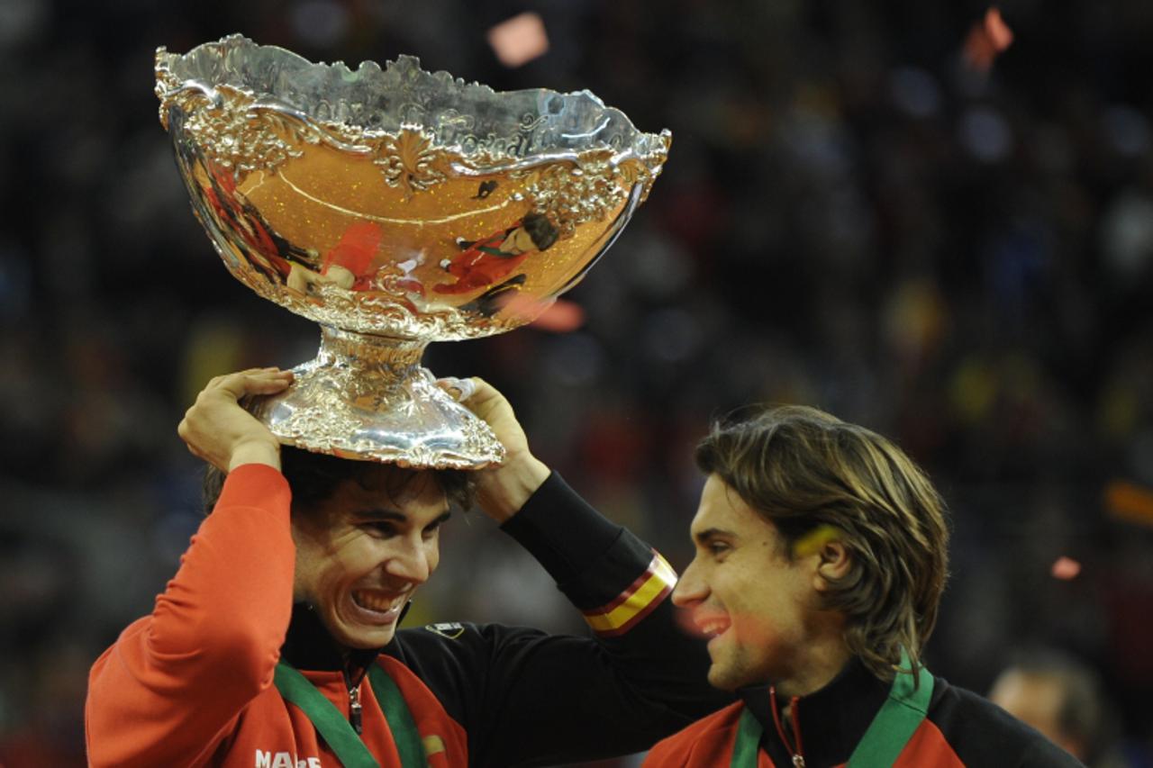 \'Spain\'s Rafael Nadal (L) celebrate holding the David Cup trophy next to tammate David Ferrer after winning the Davis Cup final against Argentina at La Cartuja Olympic stadium in Sevilla on December