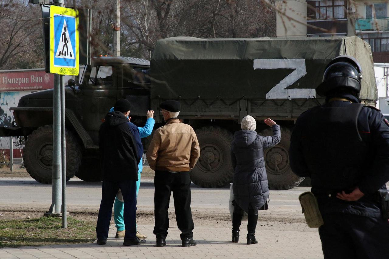 People watch as a Russian Army military truck drives along a street in Armyansk